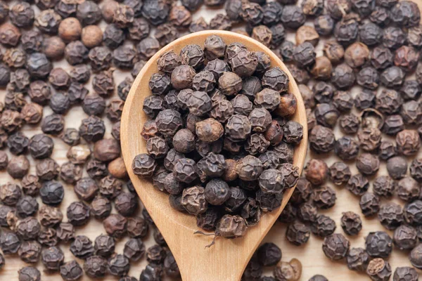 Close up of Whole Black Pepper On Wooden Spoon — стоковое фото