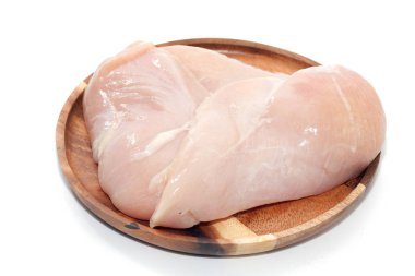 Beyaz arka planda ahşap tabakta çiğ tavuk göğsü.