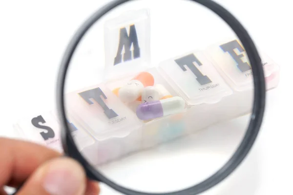 Magnifying glass with colorful pill in the box — Stock Photo, Image