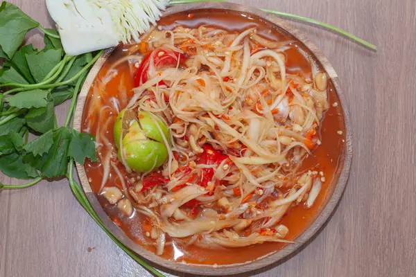 Пряный салат из папайи или сом-там в Таиланде на деревянной тарелке с овощами — стоковое фото
