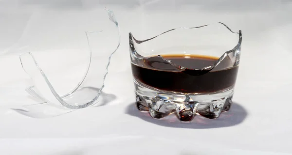 A broken whiskey glass with the remains of whiskey stands on a w — Stock Photo, Image
