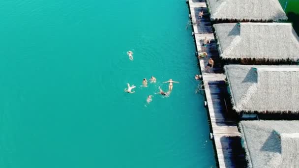 A crowd of friends bathe. Holiday. Luxurious over-water villas on tropical island resort. Aerial footage. — Stock Video