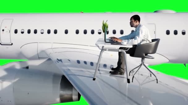 空飛ぶ飛行機に取り組んでいる若い忙しいサラリーマン。机の上にノート パソコンの画面見てアフリカ系の男性。そのクリエイティブなワークスペースの概念。緑色の画面。リアル 4 k アニメーション. — ストック動画