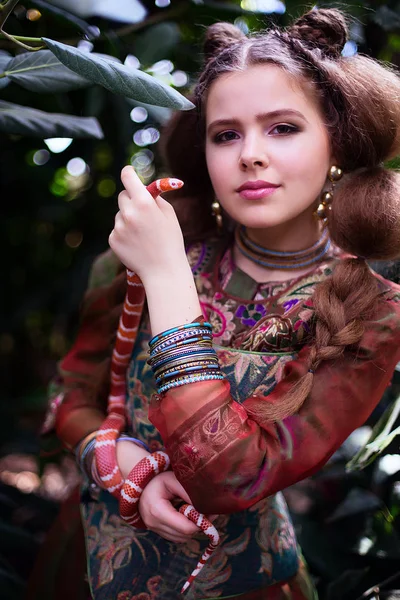 Девушка в этнической одежде в тропическом саду со змеей — стоковое фото