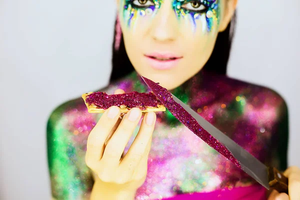 Nahaufnahme Porträt eines schönen Mädchens mit kreativem Glitzer-Make-up mit Messer und Snack mit Glitzer bedeckt — Stockfoto