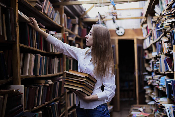 Lifestyle portrait of a lovely student girl in vintage library or bookstore