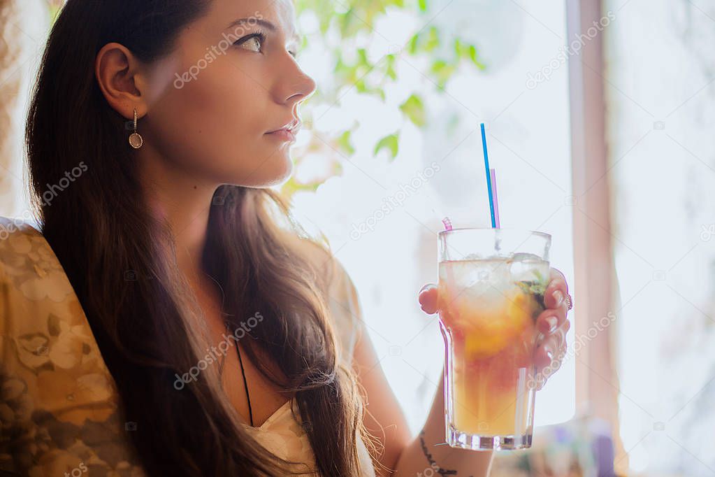 Lifestyle portrait of brunette girl in cafe holding class of cocktail or lemonade