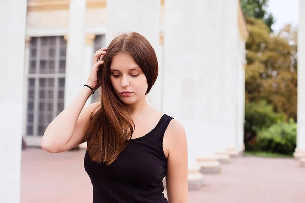 Livsstil porträtt av flicka klädd i blank svart t-shirt, jeans och pälsen poserar mot byggnaden med kolumner — Stockfoto