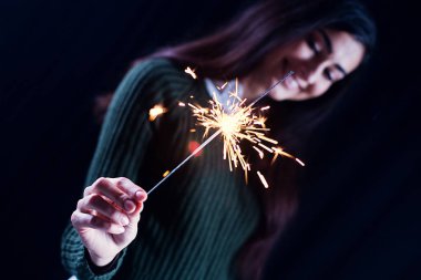 Mutlu kız gülümseyerek ve köpüklü bir havai fişek onun elinde tutan. Kız arka planda kasten mevsimlik. Noel ve yeni yıl kutlama kavramı.