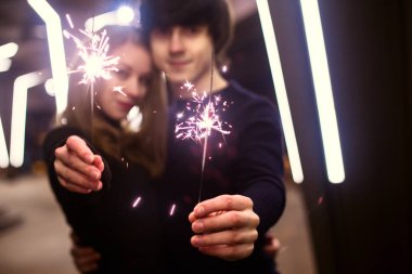 Yaşam tarzı ile arka plan ışığı çok şehir sokaklarda parlak yeni yıl havai tutarak aşık çift portresi. Noel ve yeni yıl kutlama kavramı. Kasten mevsimlik insanlar.