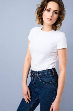 Temel beyaz t-shirt ve yüksek belli mavi jeans Studio gri arka plan üzerinde poz şık genç kız portresi