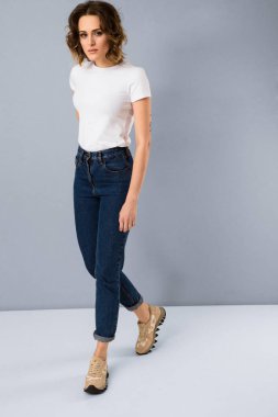 Temel beyaz t-shirt ve yüksek belli mavi jeans Studio gri arka plan üzerinde poz şık genç kız portresi