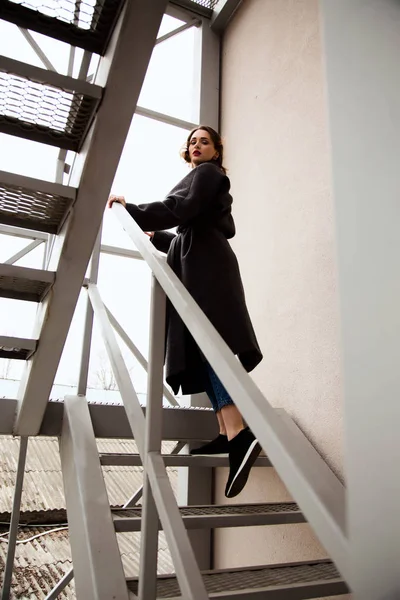 Fashion outdoor portrait of stylish  woman on the street, on the metal stairs  with view on the city, urban fashion