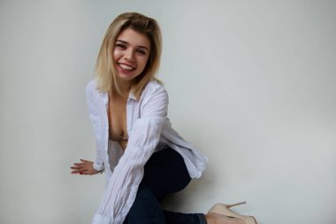 Stüdyoda çıplak iç çamaşırlarıyla poz veren sarışın güzel bir kız. Sıradan bir kot pantolon, beyaz gömlek, beyaz arka plan, gün ışığı.