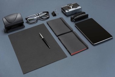 Siyah ofis aksesuarları, gözlük, eski fotoğraf makinesi ve tablet gri arka plan üzerinde bir dizi