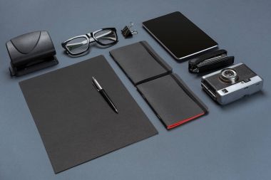 Siyah ofis aksesuarları, gözlük, eski fotoğraf makinesi ve tablet gri arka plan üzerinde bir dizi