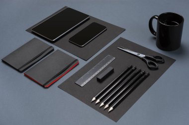 Düz boş siyah kağıt levha, siyah kırtasiye ve kahve fincanı gri masaüstü üzerinde yatıyordu. Yukarı alay