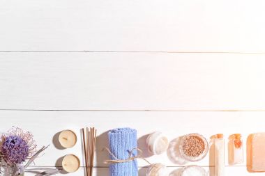Spa Ürünleri. Banyo tuzları, kuru çiçekler lavanta, sabun, mumlar ve havlu. Düz beyaz ahşap zemin, üstten görünüm üzerinde yatıyordu. Güneş parlaması