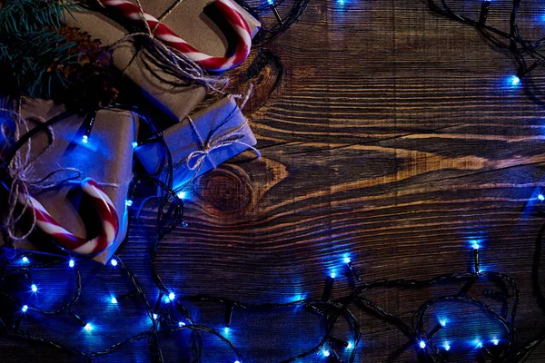 Rama de abeto con luces de Navidad, caja de regalo y bastones de caramelo sobre fondo de madera con espacio para copiar . — Foto de Stock