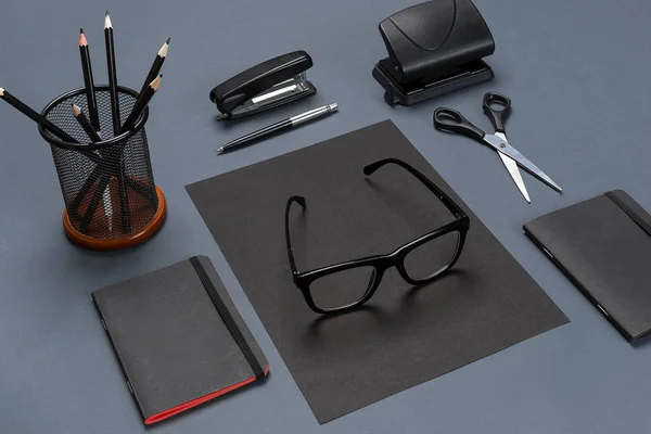 Un ensemble d'accessoires de bureau noirs, lunettes sur fond gris — Photo