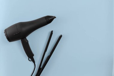 Çeşitli saç şekillendirme cihazları mavi kağıt arka planda, üstten görünüm