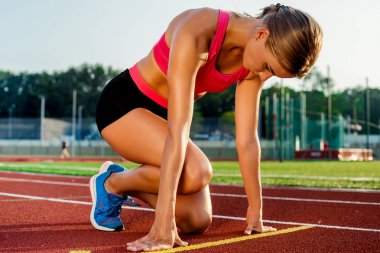 Başlama pozisyonu bir yarış pistimde başlamak için hazır, genç kadın atlet.