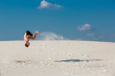 Genç adam plaj beyaz kum ve parlak mavi gökyüzü ile atlama