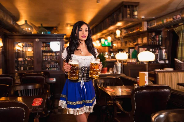 Красивая официантка в традиционной одежде и с огромным количеством пива в пабе . — стоковое фото