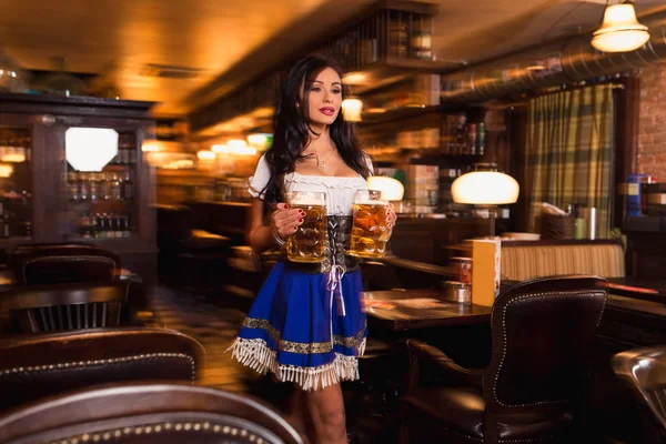 Belle serveuse vêtue de dirndl traditionnel et tenant d'énormes bières dans un pub . — Photo