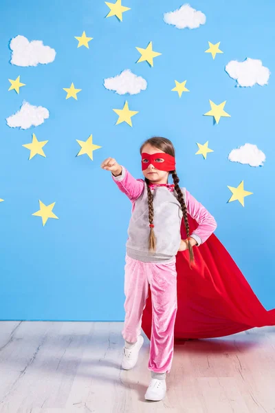 La bambina gioca a fare il supereroe. Ragazzo sullo sfondo della parete blu brillante . — Foto Stock