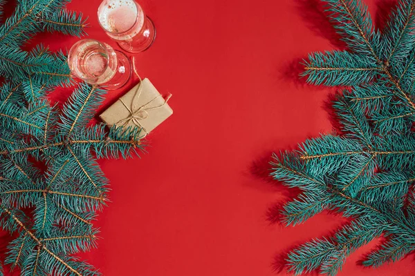 İki kadeh şampanya Noel ağacı dalı ve kırmızı bir arka plan üzerinde küçük hediye