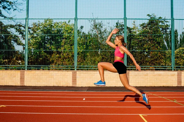 Vista lateral bela jovem jogging exercício feminino e correr na pista atlética no estádio — Fotografia de Stock