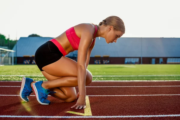 Young woman athlete at starting position ready to start a race on racetrack. — Stock Photo, Image