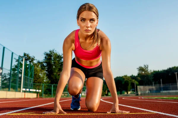 Fiatal nő sportoló a kiindulási helyzet indulásra készen a versenyt a versenypálya. — Stock Fotó
