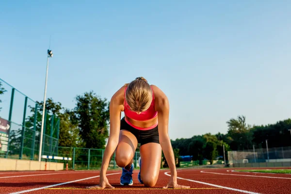 Fiatal nő sportoló a kiindulási helyzet indulásra készen a versenyt a versenypálya. — Stock Fotó