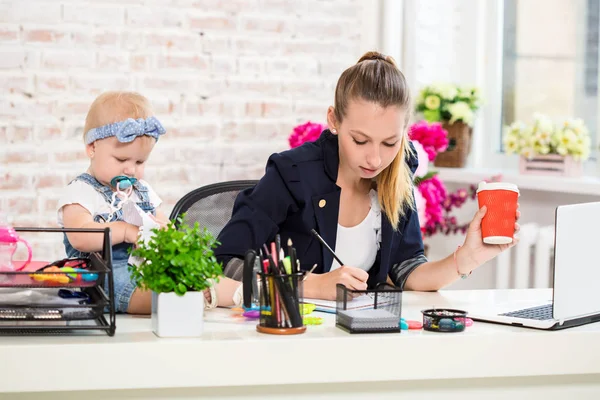 Mom and businesswoman working with laptop computer at home and playing with her baby girl.