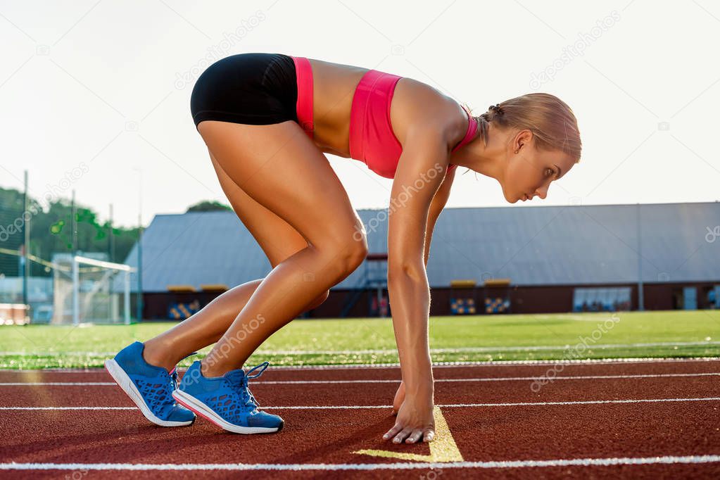 Young woman athlete at starting position ready to start a race on racetrack.