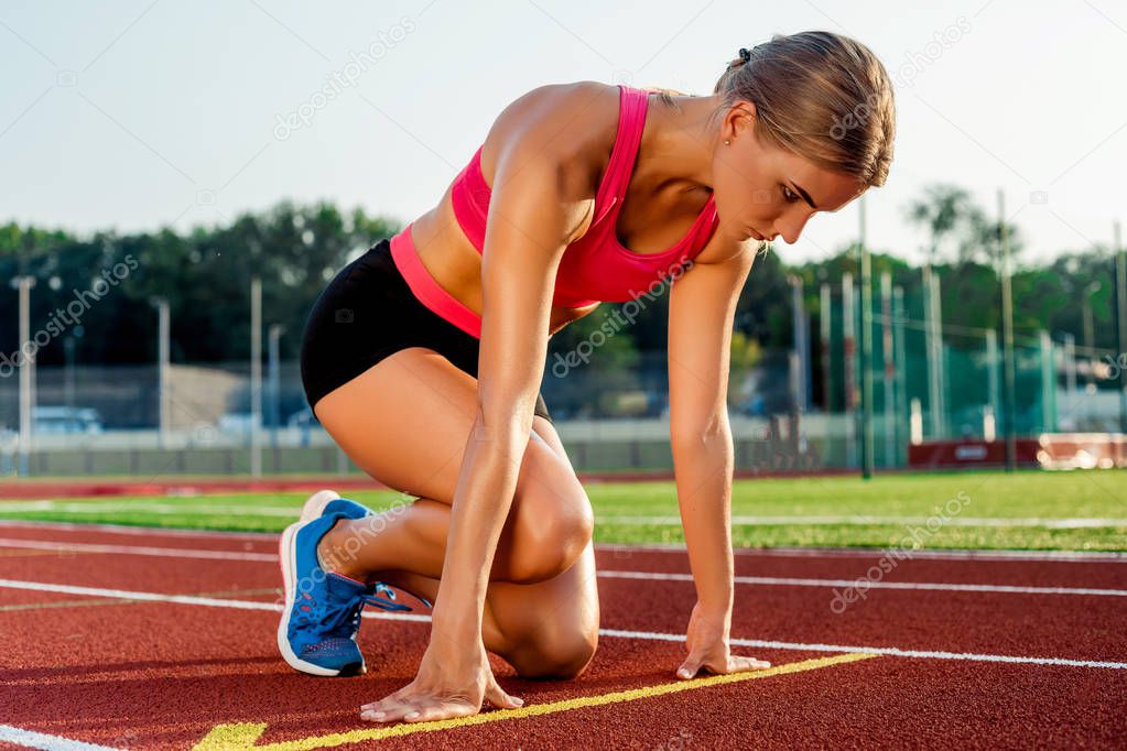 Young woman athlete at starting position ready to start a race on racetrack.