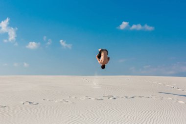Genç adam plaj beyaz kum ve parlak mavi gökyüzü ile atlama