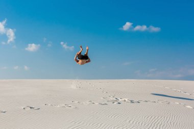 Genç adam plaj beyaz kum ve parlak mavi gökyüzü ile atlama