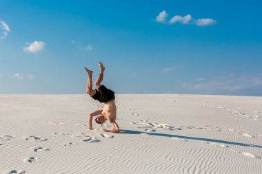 Sportif delikanlı istiyorum Nehri yakınında kum üzerinde akrobatik egzersizleri yapıyor