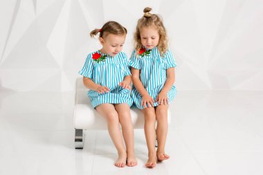 İki küçük kız arkadaşım aynı turkuaz Giydir sandalye beyaz duvarlı bir stüdyoda oturup