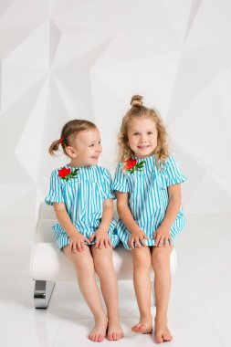 İki küçük kız arkadaşım aynı turkuaz Giydir sandalye beyaz duvarlı bir stüdyoda oturup