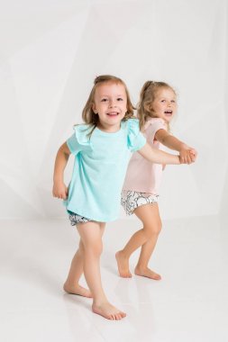 İki küçük komik ve farklı renklerde beyaz studio oynarken aynı giysili kız gülerek