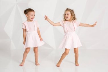 İki küçük komik gülen ve kız beyaz studio poz yavaşça pembe elbiseler