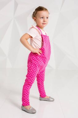 Sarı saçlı, beyaz arka plan üzerinde pembe tulum ile güzel küçük kız