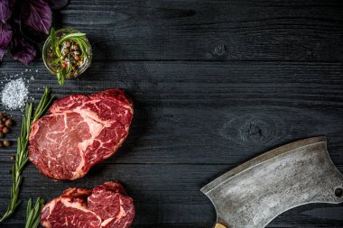 Fesleğen ve rosemary ile siyah ahşap zemin üzerine eti için balta sapı ile taze çiğ et. Üstten Görünüm