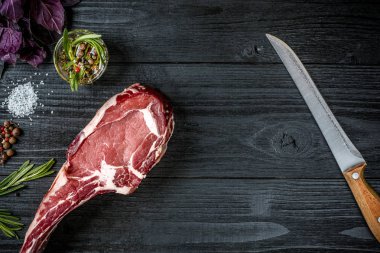 Fesleğen ve rosemary ile siyah ahşap zemin üzerine Ahşap Saplı bıçak sapı ile taze çiğ et. Üstten Görünüm