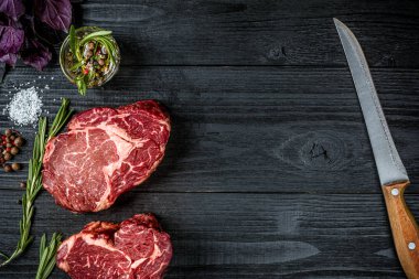 Fesleğen ve rosemary ile siyah ahşap zemin üzerine Ahşap Saplı bıçak sapı ile taze çiğ et. Üstten Görünüm