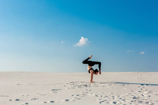 Junge Frau übt Handstand am Strand mit weißem Sand und strahlend blauem Himmel — Stockfoto